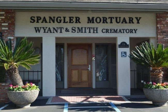 A cream-colored building with a dark wooden arched door and a sign reading 