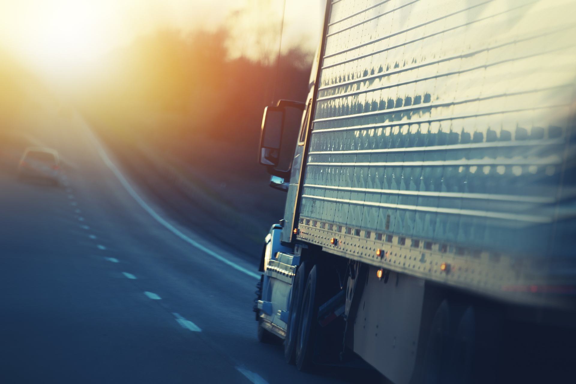 A semi truck is driving down a highway at sunset.