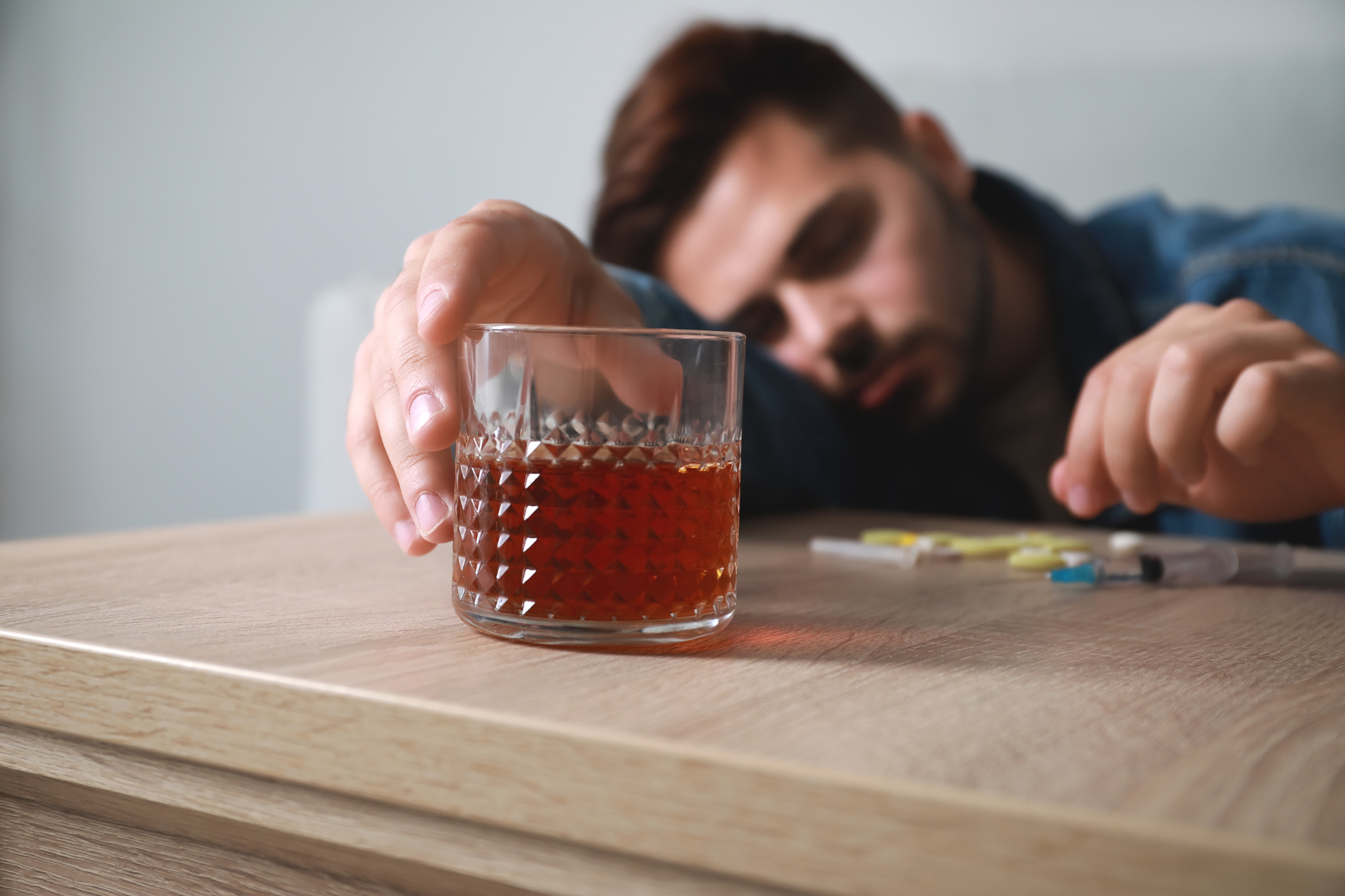 A man is sitting at a table with a glass of alcohol and a syringe.