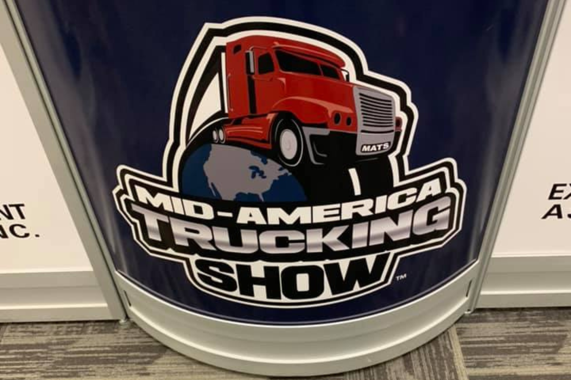 A sign for the mid-america trucking show with a red truck on a globe.