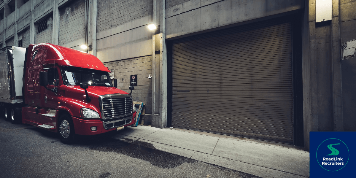 A red semi truck is parked in front of a garage door.