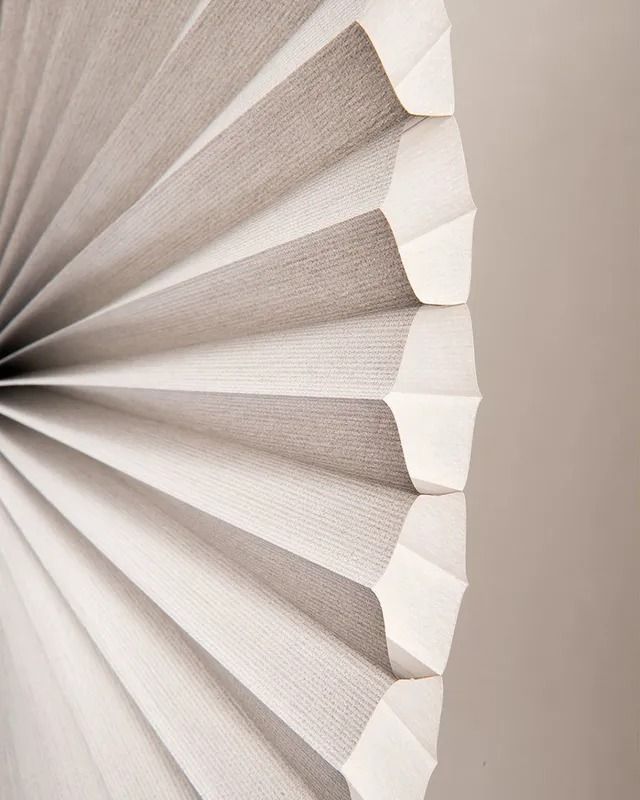 A close up of a white pleated blind on a window.