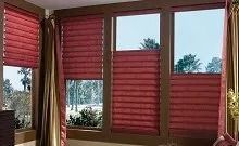 A room with three windows and red blinds on them.