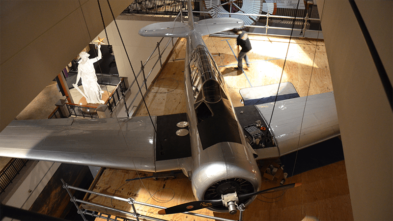 An airplane is hanging from the ceiling in a museum.