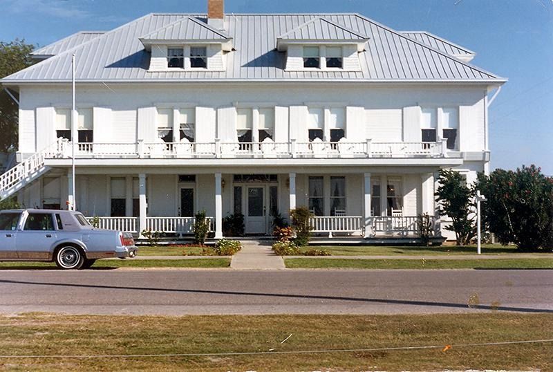A white car is parked in front of a large white house