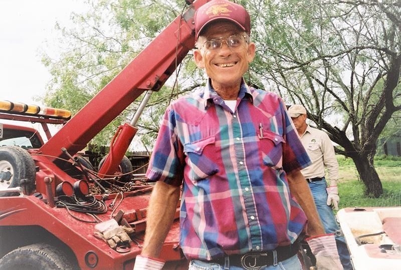 A man in a plaid shirt is standing next to a tow truck