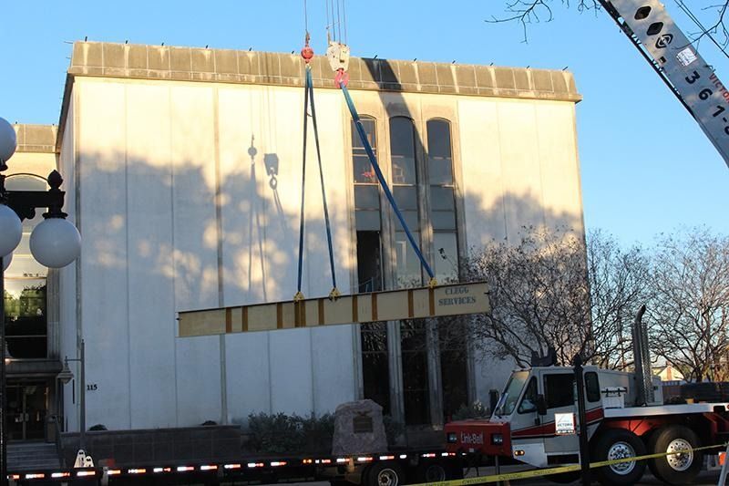 A crane is lifting a large piece of wood in front of a building