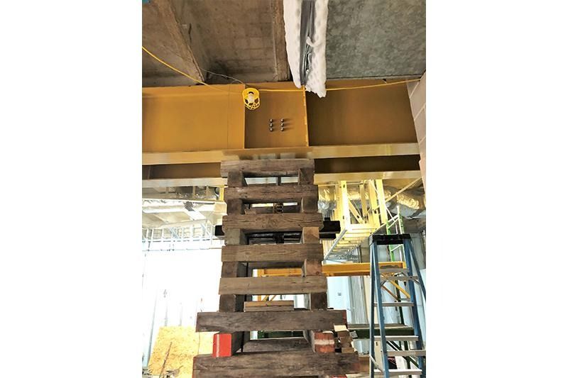 A wooden ladder is going up to the ceiling of a building.