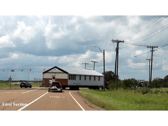 A car is driving down a road next to a house on a trailer.