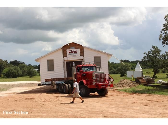 A red truck is carrying a white building that says craig