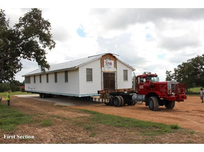 A red truck is carrying a white house in the first section