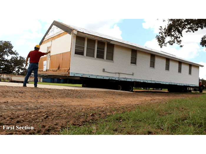A man is standing in front of a large house on a trailer.