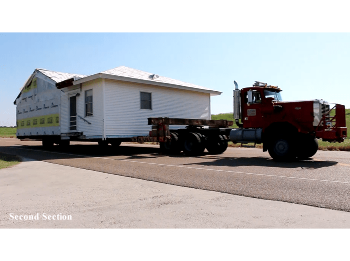 A red truck is pulling a house down a road