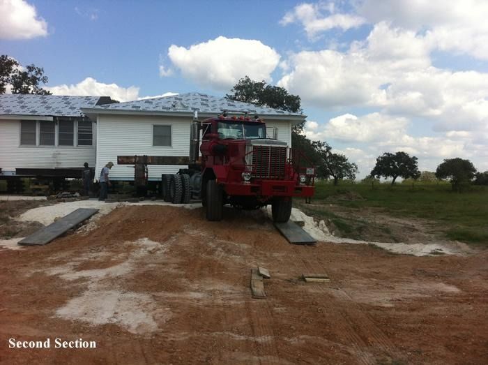 A red truck is parked in front of a house that is being moved