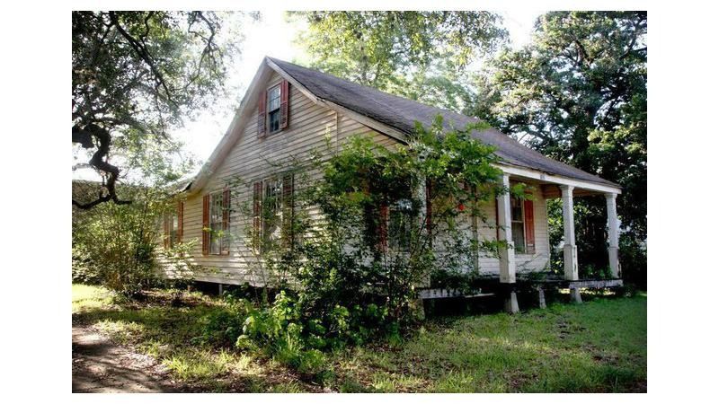 A small white house with a porch surrounded by trees