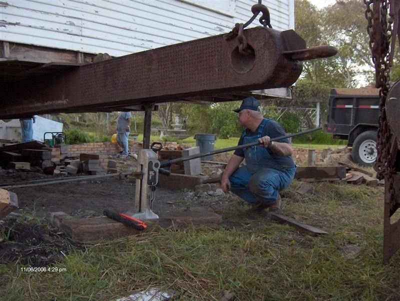 A man is squatting down under a large piece of metal.