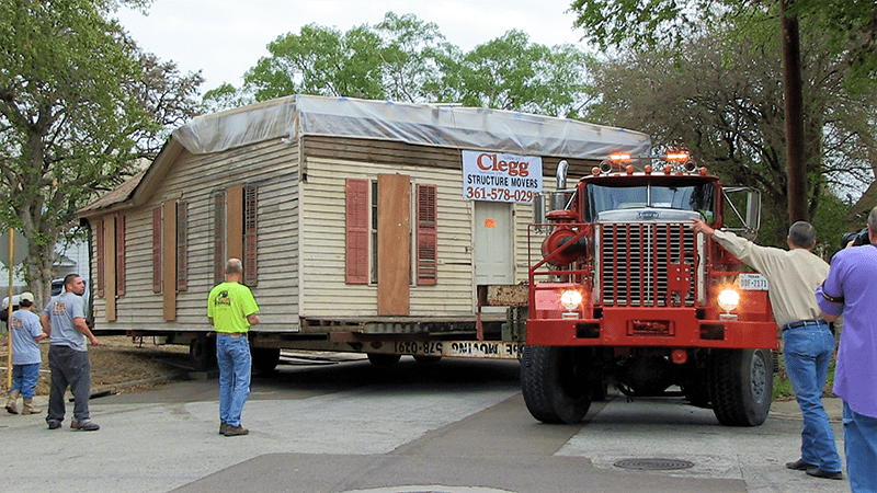 A house is being moved by a red truck that says cleo moving services