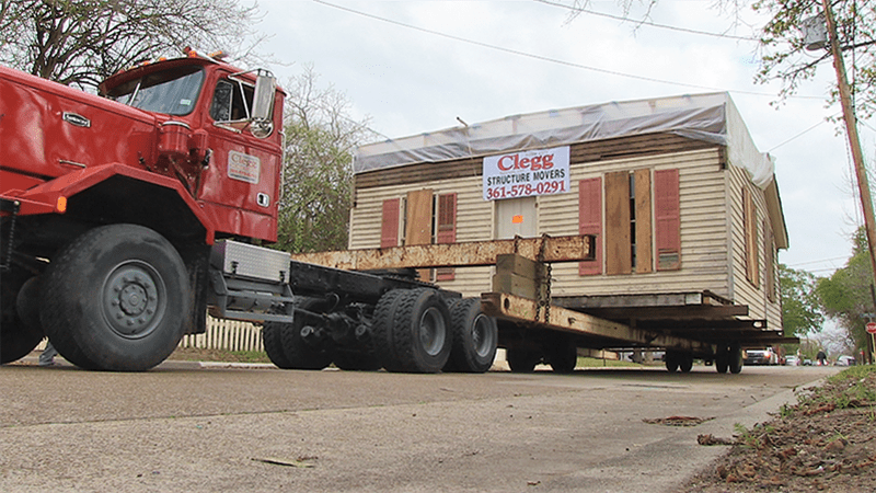 A large red truck is carrying a house on a trailer.