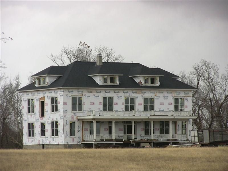 A large white house with a black roof is under construction