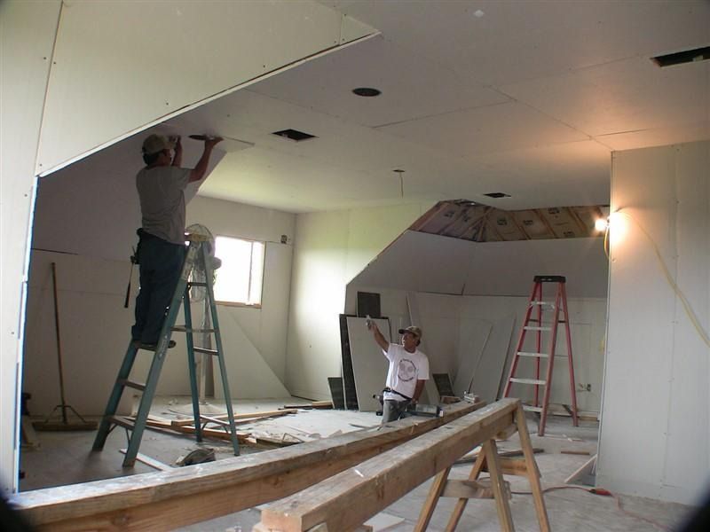 Two men are working on a ceiling in a room