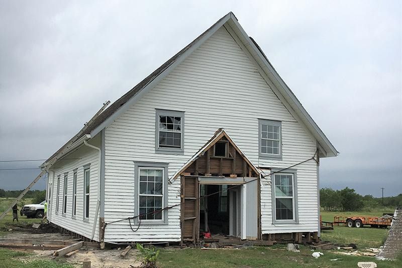 A large white house is being demolished in a field.