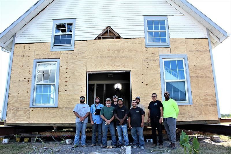 A group of men are standing in front of a house that is being moved.