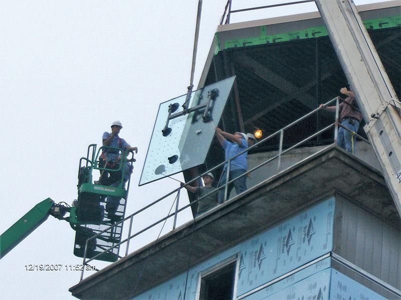 A crane is lifting a piece of glass on top of a building