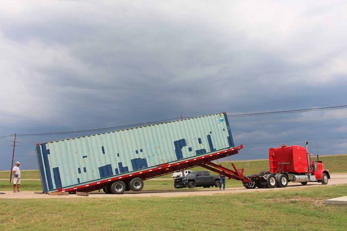 A semi truck is carrying a shipping container on a flatbed trailer.