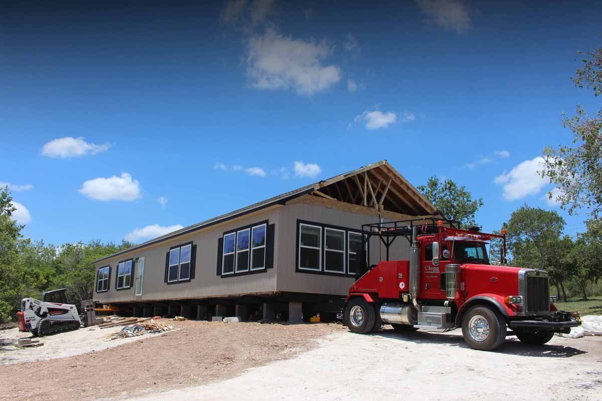 A red semi truck is parked in front of a house under construction.