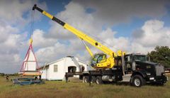 A yellow crane is lifting a piece of wood in front of a house.