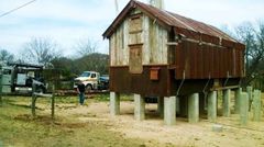 A man is standing in front of a rusty building on stilts.