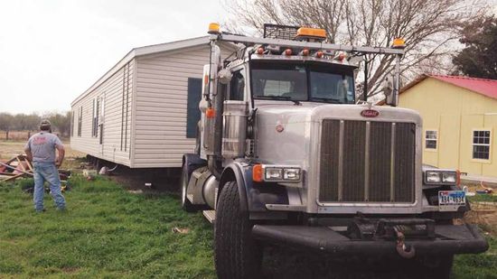 A semi truck is carrying a mobile home in a grassy field.