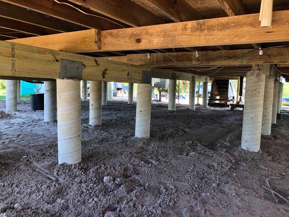 The underside of a house under construction with concrete pillars and wooden beams.