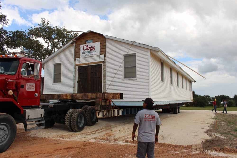 A man stands in front of a truck that is moving a house