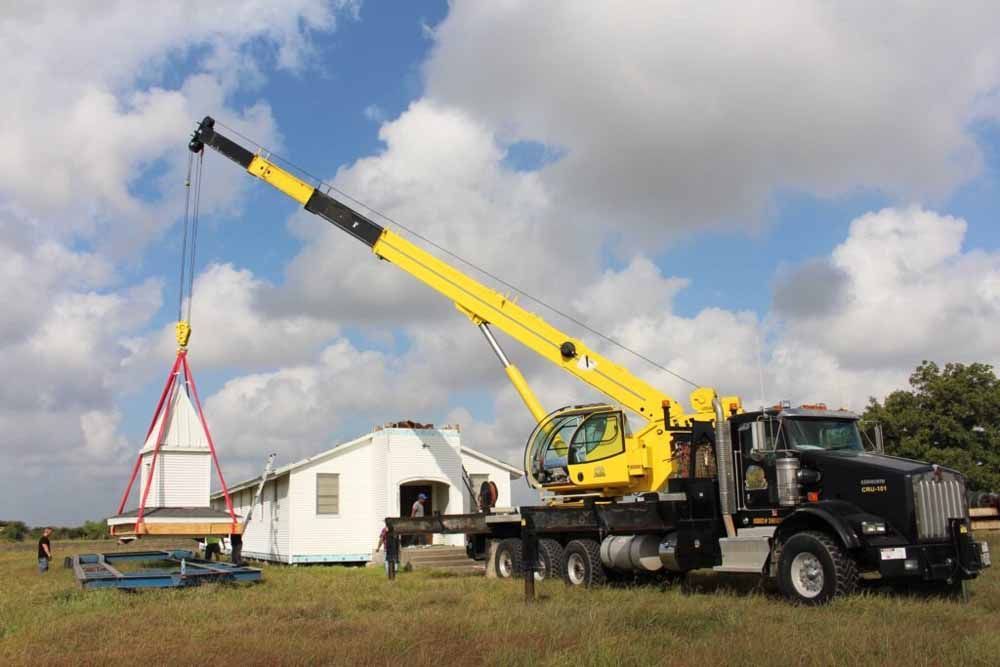 A yellow crane is lifting a piece of wood in a field.