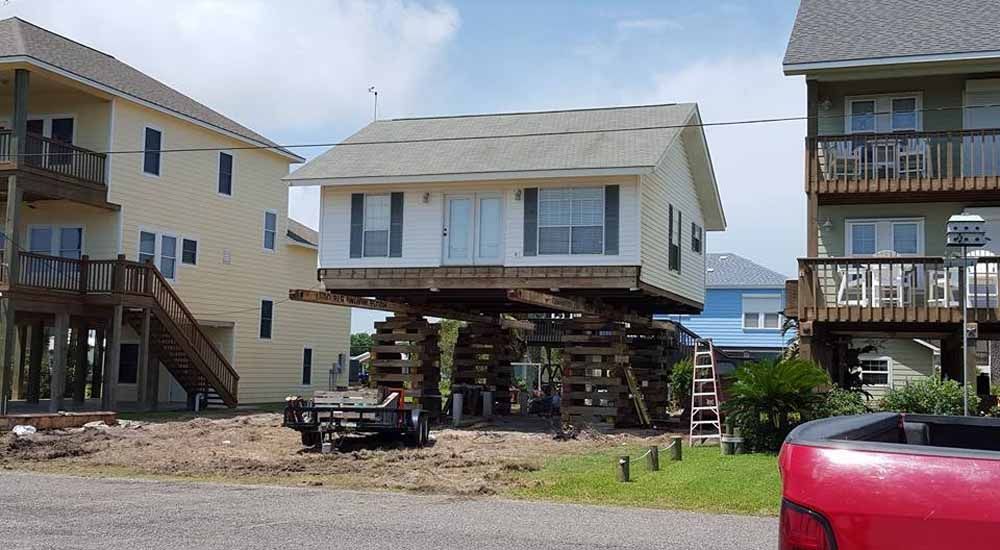 A red truck is parked in front of a house that is being moved.