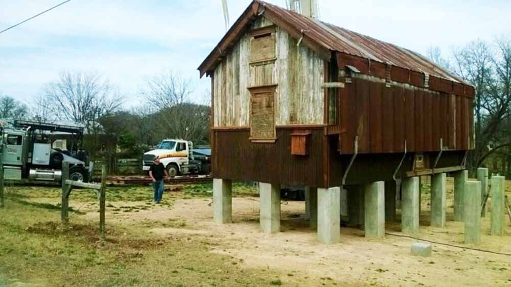 A man is standing in front of a rusty building on stilts.