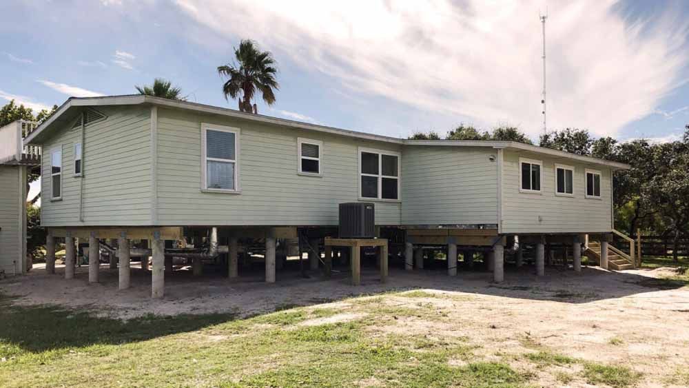A large white house on stilts with a palm tree in the background.