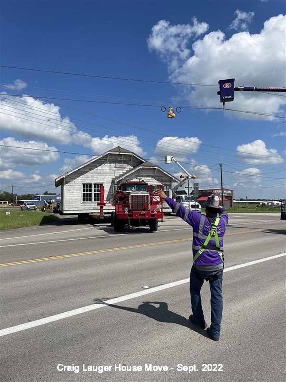 A man is standing on the side of the road while a house is being moved.