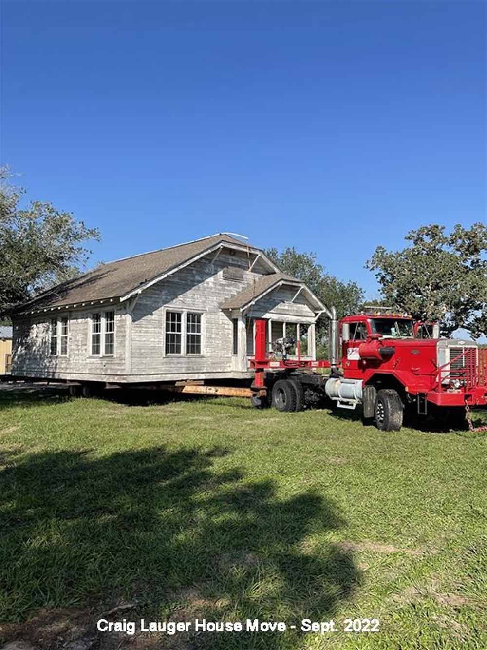 A red truck is carrying a house on a trailer.
