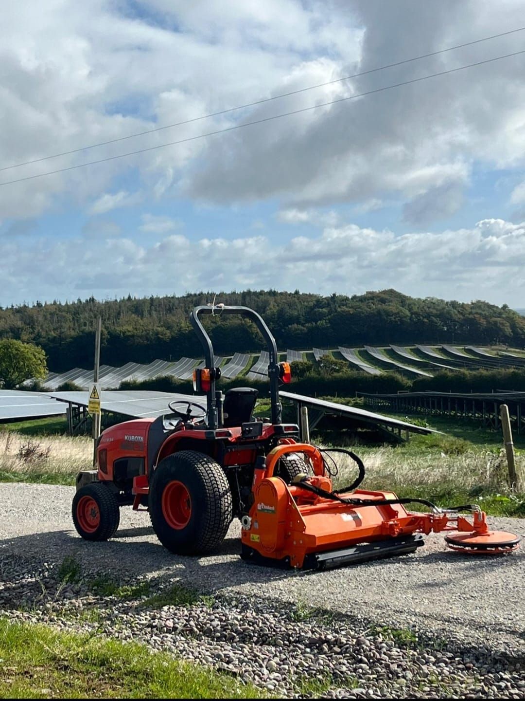 A small orange tractor is parked on the side of a gravel road.