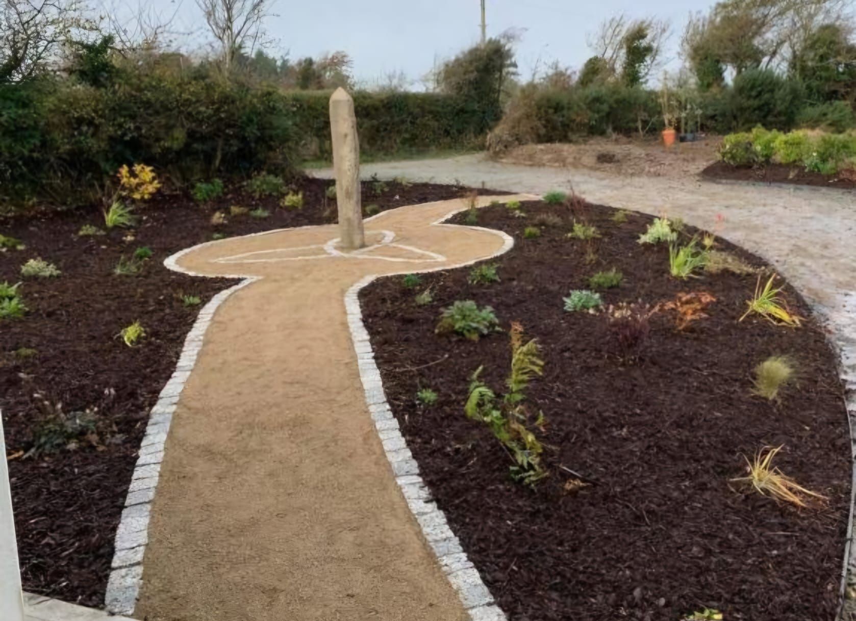 A path going through a garden with a stone in the middle.