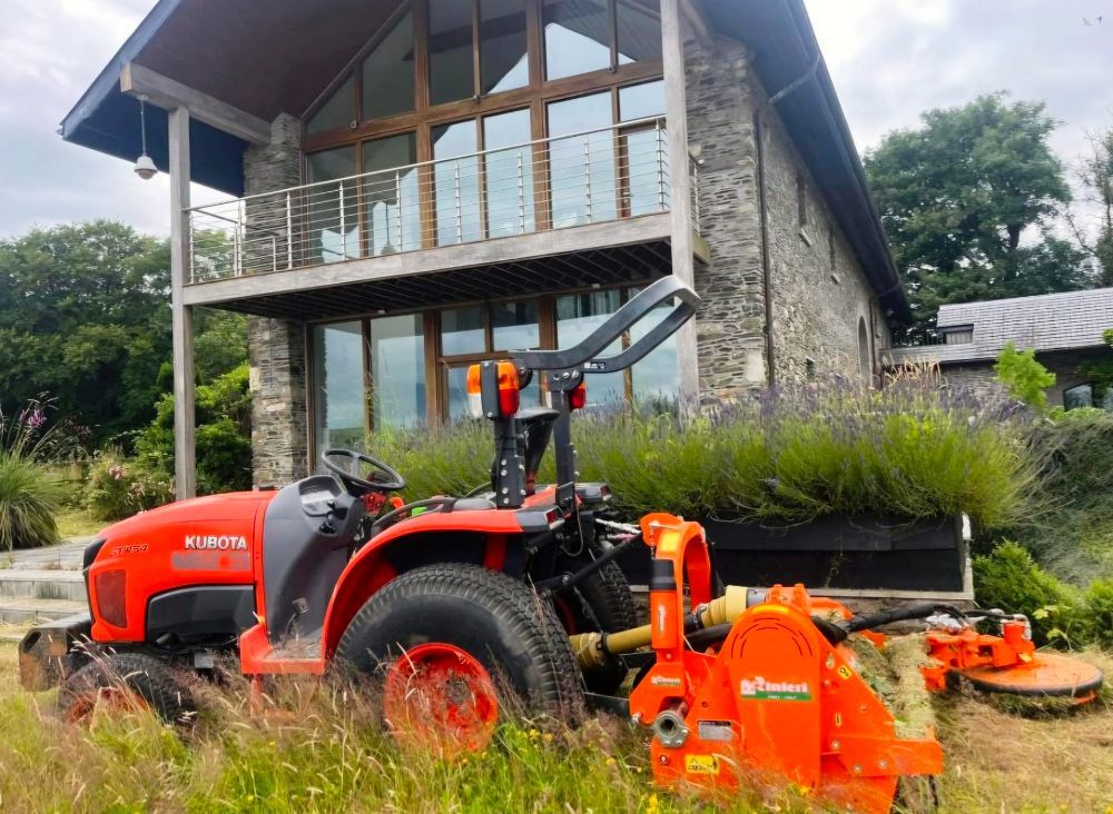 A red tractor is parked in front of a large stone house.