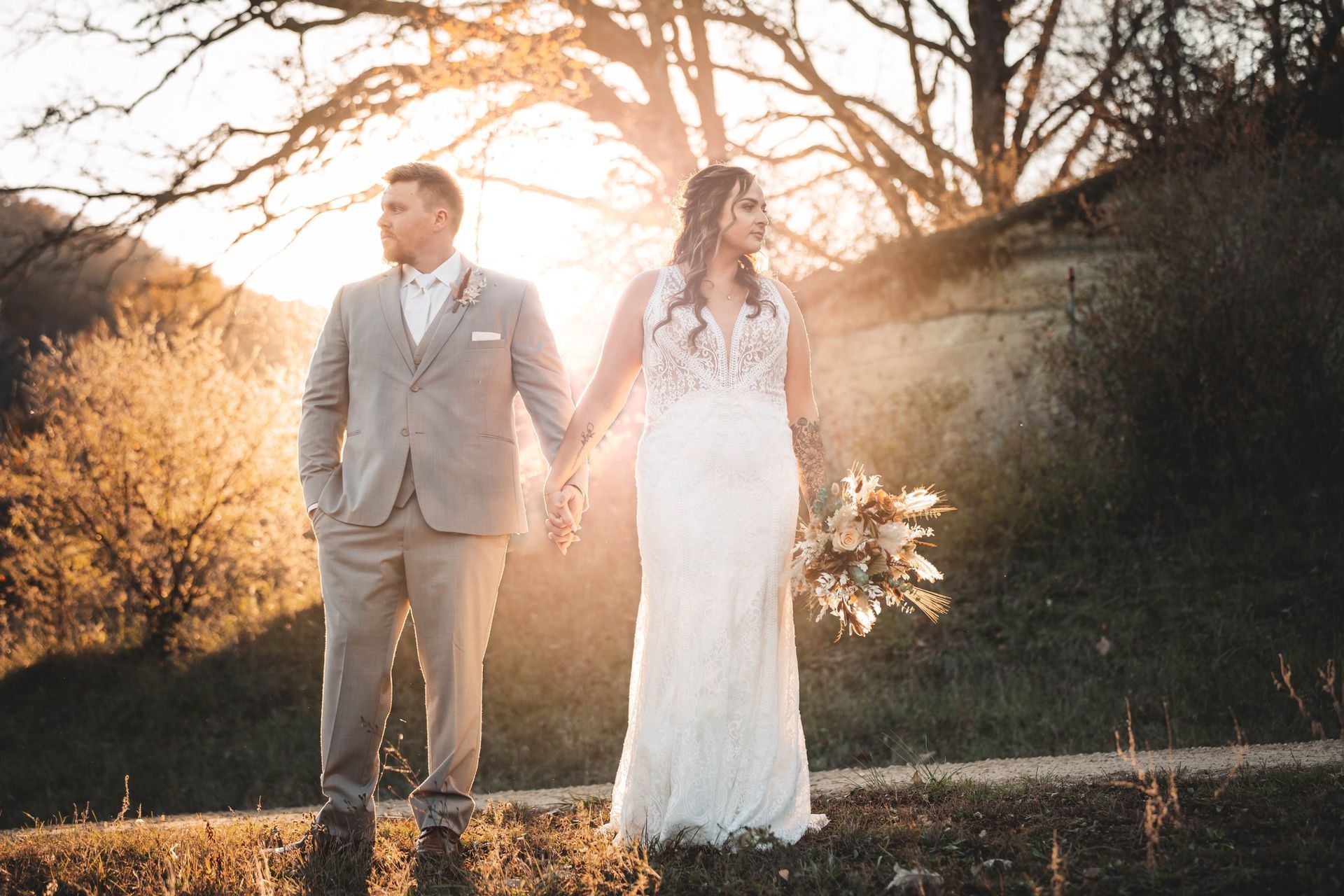 A bride and groom are holding hands in a field at sunset.