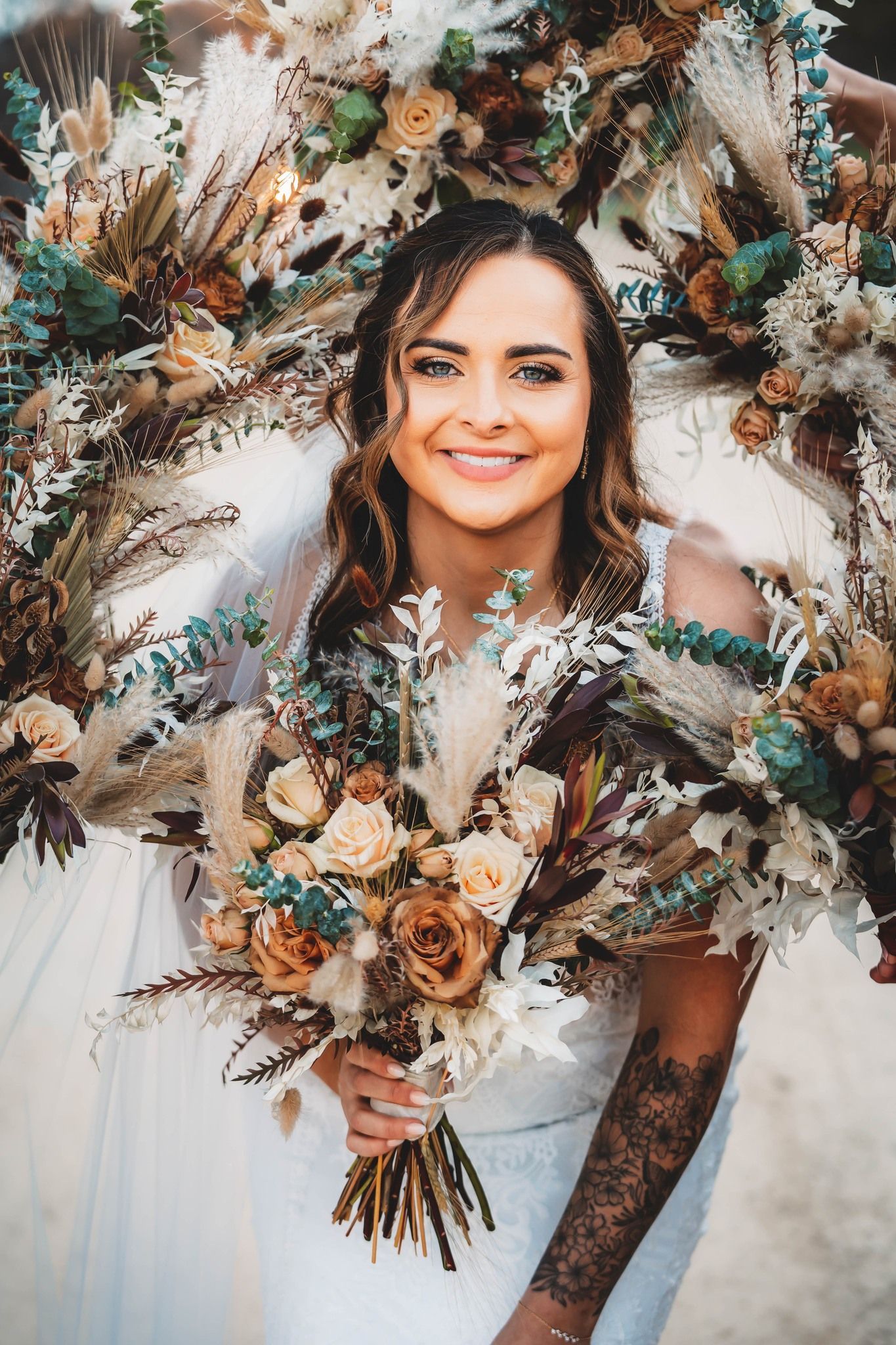 A bride in a white dress is holding a bouquet of dried flowers.