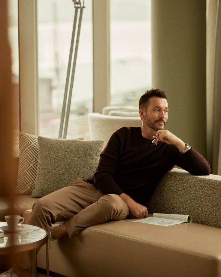 A man is sitting on a couch looking out a window.