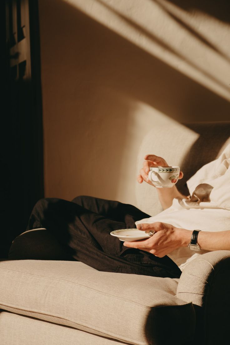 A woman is sitting on a couch holding a cup of coffee.