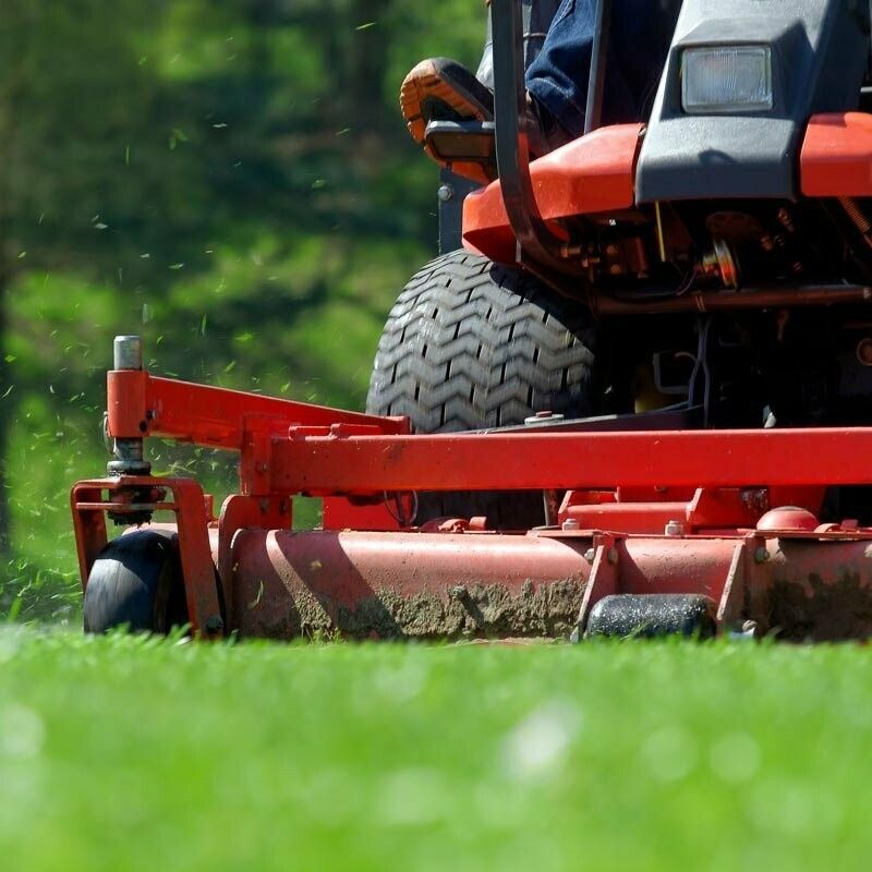 A Person is Riding a Red Lawn Mower on a Lush Green Field — Jacksons Mower Centre in Mackay, QLD