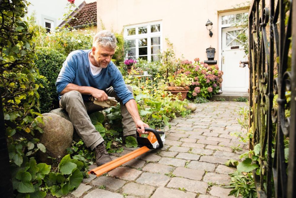 A Man is Sitting on a Rock in a Garden Using a Tape Measure — Jacksons Mower Centre in Mackay, QLD
