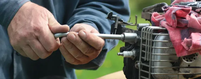A Man is Working on a Lawn Mower With a Wrench — Jacksons Mower Centre in Mackay, QLD
